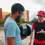 Two men talking. One is holding a motorycle helmet.