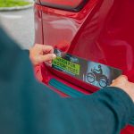 Person placing a 'watch for motorcycles' bumper sticker on a red car.